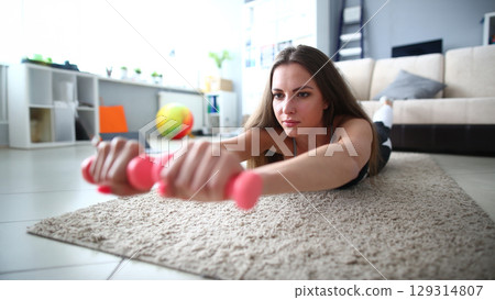 Woman engages in home workout routine focusing on strength and endurance using pink dumbbells in a cozy living room setting Woman engages in home workout routine focusing on strength and endurance using pink dumbbells in a cozy living room setting 129314807