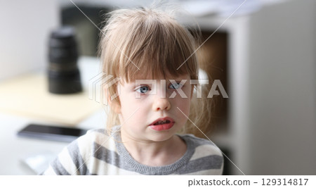Young child with striking blue eyes engages in playful conversation in a cozy home environment during midday hours 129314817