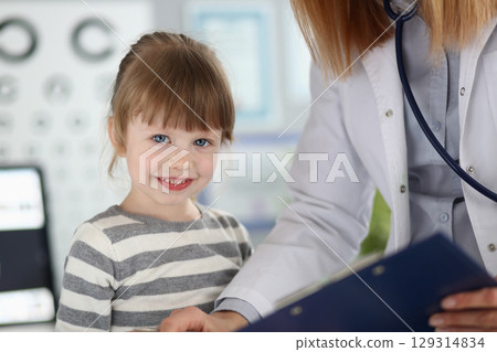 Smiling child during a checkup in a bright clinic with a caring doctor wearing a white coat in a friendly atmosphere Smiling child during a checkup in a bright clinic with a caring doctor wearing a white coat in a friendly atmosphere 129314834