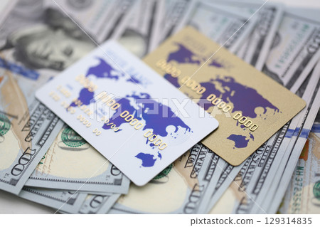 Colorful credit cards resting on a stack of hundred-dollar bills during a sunny afternoon in a bustling city market 129314835