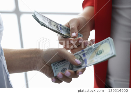 Exchange of cash between two people in a modern setting with focus on hands and bills 129314900