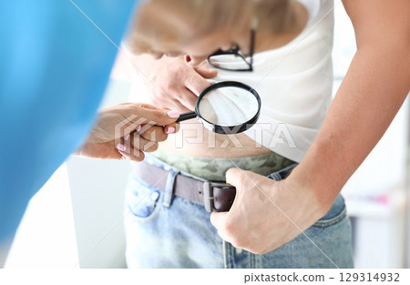 Curious examination of a man's midsection using a magnifying glass in a bright indoor setting during a casual moment 129314932