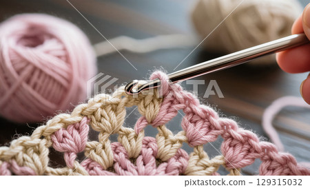 Close-up of crochet hook working with pink and beige yarn, creating a delicate handmade pattern. Cozy craft process in detail. Close-up of crochet hook working with pink and beige yarn, creating a delicate handmade pattern. Cozy craft process in detail. 129315032