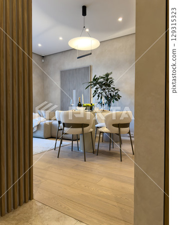 A stylish dining area with modern furniture and a minimalist design. A large pendant light hangs over a round table, creating an inviting atmosphere for a chic and cozy home setting 129315323