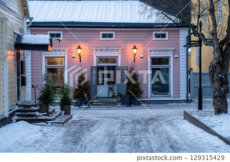 Charming pink wooden house with Christmas trees and lanterns in snowy street 129315429