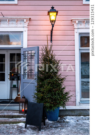 Outdoor Christmas tree with fairy lights by vintage pink wooden house Outdoor Christmas tree with fairy lights by vintage pink wooden house 129315431