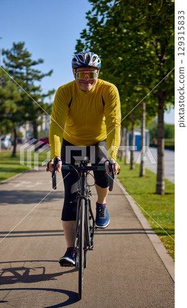 Older male cyclist smiling while riding road bike in sunny park 129315833