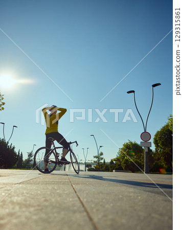 Man in yellow cycling outfit stretching arms while standing with road bike 129315861