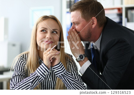 Office gossip thrives as a man shares a secret, sparking curiosity and connection with a woman in a modern workspace 129316523