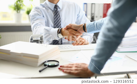 Business professionals engaging in a handshake to finalize a deal in a bright, modern office setting during the morning 129316552