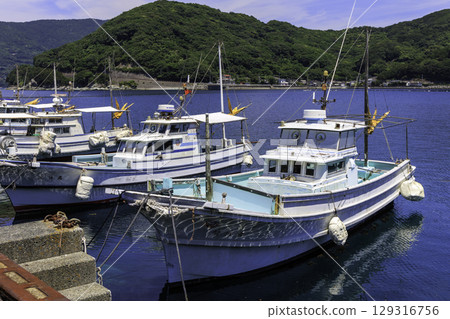 A calm summer harbor scene with fishing boats moored at the Inoura branch of Misaki Fisheries Cooperative Association in Ehime Prefecture and the blue sea A calm summer harbor scene with fishing boats moored at the Inoura branch of Misaki Fisheries Cooperative Association in Ehime Prefecture and the blue sea 129316756