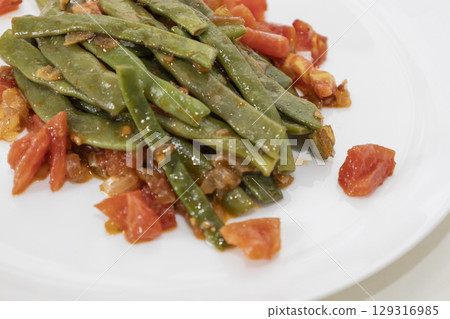 Fried green beans with tomato and onion pieces. Tasty meal with french bean on dinner or lunch on the white plate 129316985