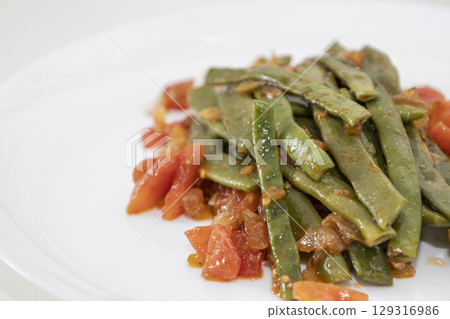 Fried green beans with tomato and onion pieces. Tasty meal with french bean on dinner or lunch on the white plate 129316986