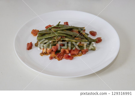 Fried green beans with tomato and onion pieces. Tasty meal with french bean on dinner or lunch on the white plate Fried green beans with tomato and onion pieces. Tasty meal with french bean on dinner or lunch on the white plate 129316991