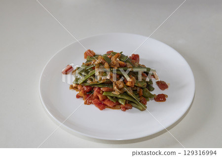 Fried green beans with tomato and onion pieces. Tasty meal with french bean on dinner or lunch on the white plate Fried green beans with tomato and onion pieces. Tasty meal with french bean on dinner or lunch on the white plate 129316994