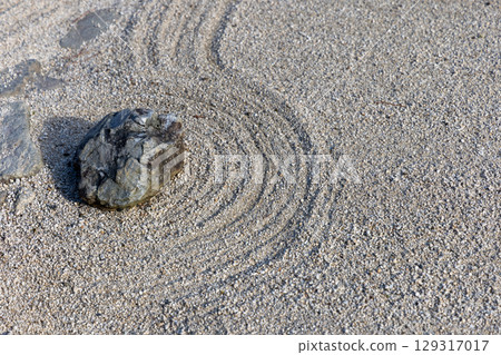 Stone placed in raked gravel with curved lines in a dry landscape Japanese rock garden 129317017