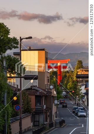 Red torii of Heian-jingu Shrine rising beyond rooftops in Kyoto during golden hour with calm traffic 129317030