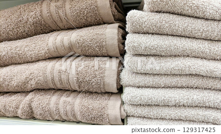 Several stacks of soft, neutral-colored towels in shades of beige and gray, neatly folded and displayed on store shelf. Perfect for concepts related to home textiles, bathroom goods or retail Several stacks of soft, neutral-colored towels in shades of beige and gray, neatly folded and displayed on store shelf. Perfect for concepts related to home textiles, bathroom goods or retail 129317425