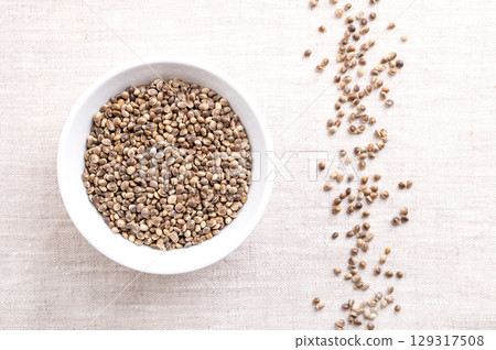 Whole hemp seeds in a white bowl on linen. Raw, unhulled fruits of industrial hemp, a Cannabis sativa cultivar, low on THC, and grown for consumption. Crunchy texture, nutty flavor, used for toppings. Whole hemp seeds in a white bowl on linen. Raw, unhulled fruits of industrial hemp, a Cannabis sativa cultivar, low on THC, and grown for consumption. Crunchy texture, nutty flavor, used for toppings. 129317508