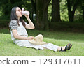 A young woman sitting on the grass and drinking water from her own bottle 129317611