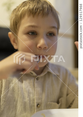 Blond boy eating with fork and looking away from camera Blond boy eating with fork and looking away from camera 129317988