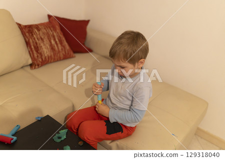 Child playing with modeling clay on sofa at home: developing fine motor skills 129318040