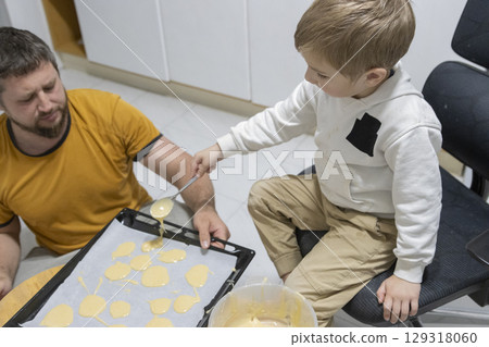 Father and son baking cookies together in kitchen: pouring batter onto baking sheet 129318060