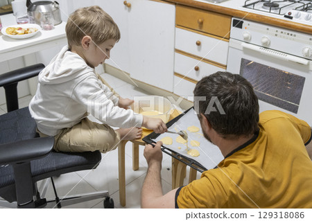 Father and son preparing cookies on baking tray in kitchen 129318086