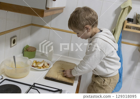 Young child cutting fruit on wooden board in kitchen 129318095