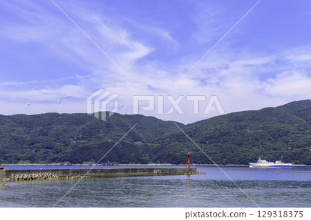 View of the port and ferry in Ikata Town with the windmills and red lighthouse of the Sada Misaki Peninsula 129318375