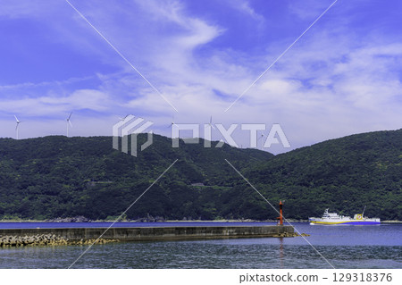 View of the port and ferry in Ikata Town with the windmills and red lighthouse of the Sada Misaki Peninsula 129318376