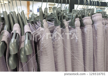 Clothing rack filled with light purple trousers on hangers. Light summer clothing sales concept Clothing rack filled with light purple trousers on hangers. Light summer clothing sales concept 129318701