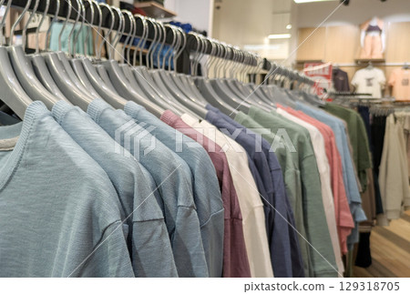 Long shot of clothing rack in store, displaying variety of different colored cotton t-shirts and tops 129318705