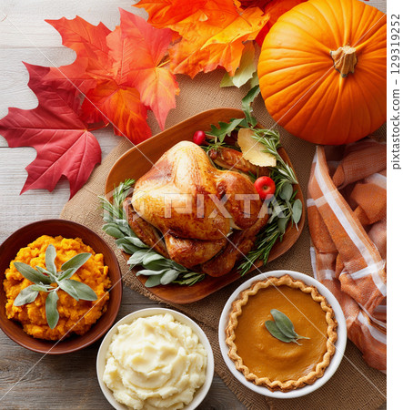 Delicious Thanksgiving feast with roast turkey, sides, and pumpkin pie surrounded by autumn decorations on a wooden table Delicious Thanksgiving feast with roast turkey, sides, and pumpkin pie surrounded by autumn decorations on a wooden table 129319252