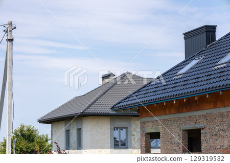 New residential buildings showcase modern roofing designs under a bright blue sky in a peaceful suburban neighborhood New residential buildings showcase modern roofing designs under a bright blue sky in a peaceful suburban neighborhood 129319582