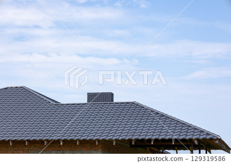 Work on a new roof is nearly complete on a residential building, surrounded by open space and a few clouds in the bright blue sky Work on a new roof is nearly complete on a residential building, surrounded by open space and a few clouds in the bright blue sky 129319586