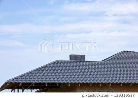 A residential building featuring a modern roof design with textured shingles under a clear blue sky during daytime A residential building featuring a modern roof design with textured shingles under a clear blue sky during daytime 129319587