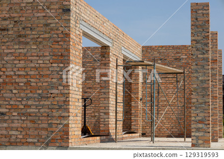 Brick walls are being erected for a new residential building with scaffolding present at the construction site on a sunny day Brick walls are being erected for a new residential building with scaffolding present at the construction site on a sunny day 129319593