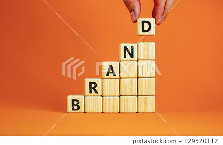 Brand symbol. Concept word Brand on beautiful wooden blocks. Beautiful orange table orange background. Businessman hand. Business brand concept. Copy space. 129320117