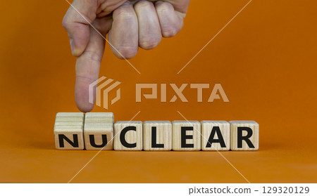 Nuclear or clear symbol. Businessman turns a cube and changes the word 'nuclear' to 'clear'. Beautiful orange background. Nuclear or clear and business concept. Copy space. Nuclear or clear symbol. Businessman turns a cube and changes the word 'nuclear' to 'clear'. Beautiful orange background. Nuclear or clear and business concept. Copy space. 129320129