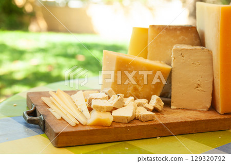 Assortment of hard cheeses cut into slices and chunks on outdoor picnic table 129320792