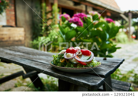 Plate of salad sits on a wooden table outside 129321041