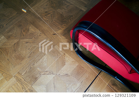 Red chair with a black handle sits on a wooden floor 129321109