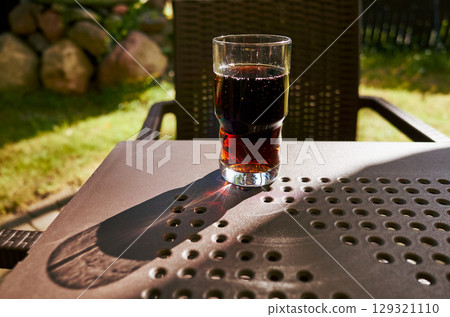 Glass of dark colored liquid sits on a table in the shade 129321110