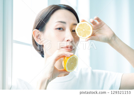 燈光下，一位透明女子雙手捧著檸檬。特寫照片中，她正看著鏡頭。 129321153