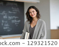 Smiling teacher holding books in classroom, educating, and smiling confidently with her warm 129321520