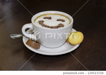 A cup of coffee with candy and biscuits  on dark background.   Smile is depicted on the coffee from the foam. Coffe - smile 129321538