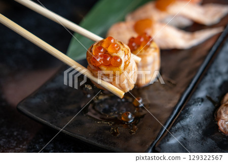 Chopsticks holding Ikura with grilled Salmon Roll Chopsticks holding Ikura with grilled Salmon Roll 129322567