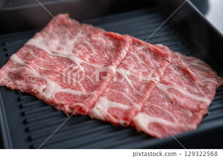 A close-up shot of sliced raw meat, arranged on a plate, ready to be cooked in a hot pot A close-up shot of sliced raw meat, arranged on a plate, ready to be cooked in a hot pot 129322568