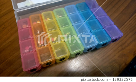 Weekly pill organizer with color-coded compartments on wooden surface 129322575